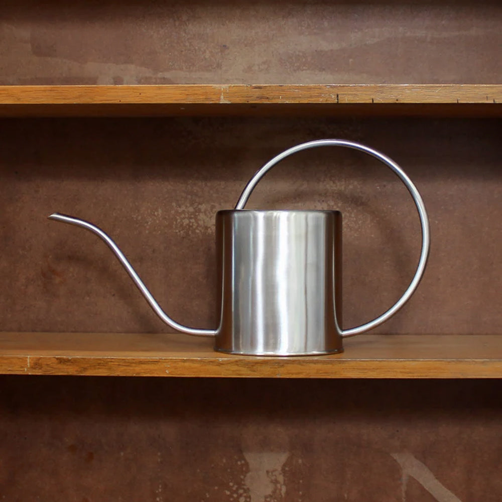 Stainless steel watering can on a wooden shelf with a brown background
