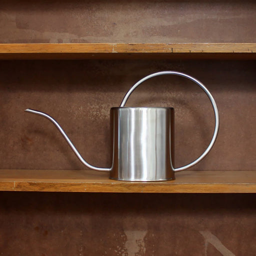 Stainless steel watering can on a wooden shelf with a brown background