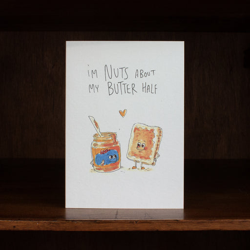 Well Drawn greeting card with cartoon characters of a jar of peanut butter and a piece of bread with jelly, text 'I'm nuts about my butter half', on a white background.