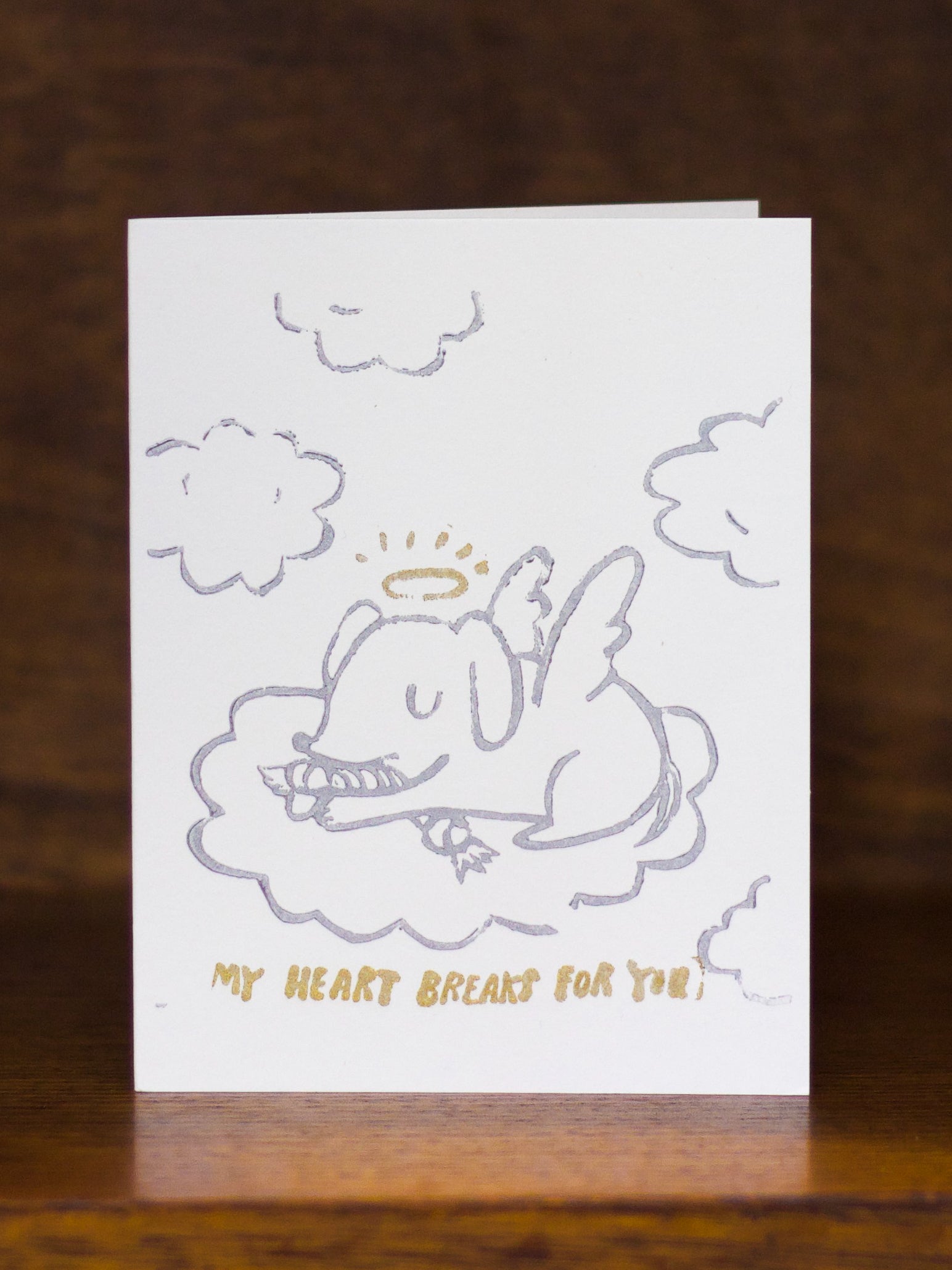 Pet Sympathy Greeting card by Ghost Academy with an illustration of a dog in clouds and text 'My heart breaks for you' on a wooden surface.