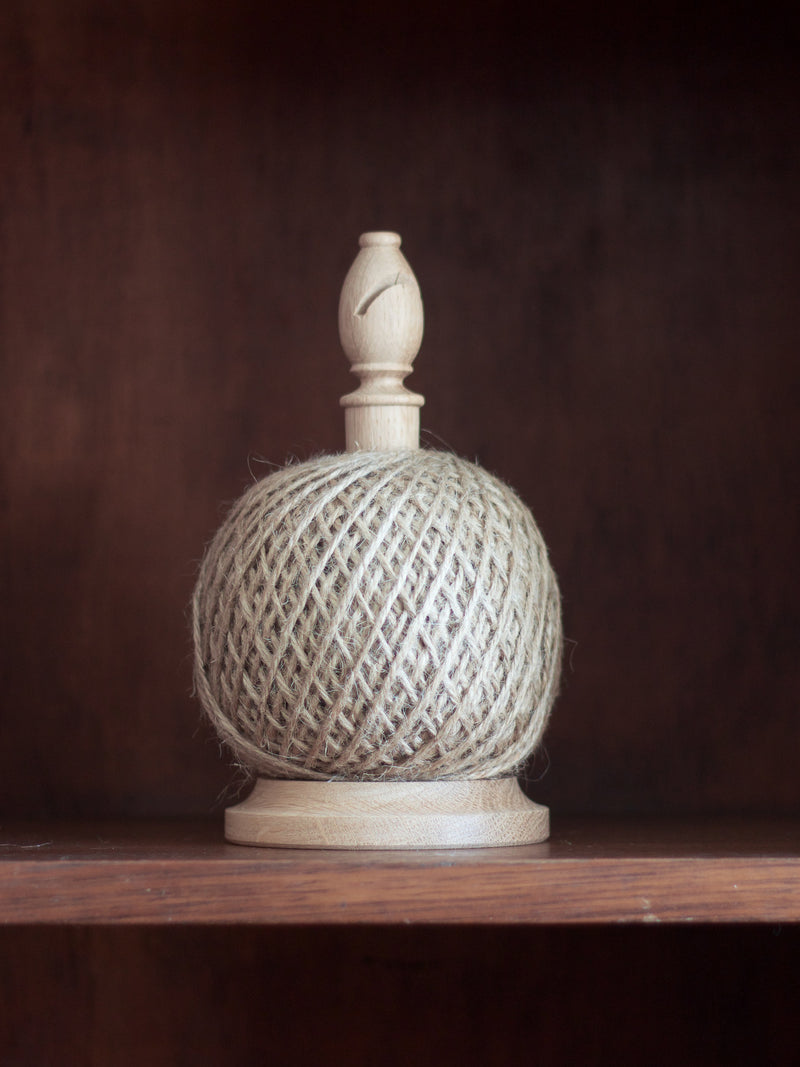 Ball of twine on wooden standing with butter in top with woven top and wooden base on a dark background
