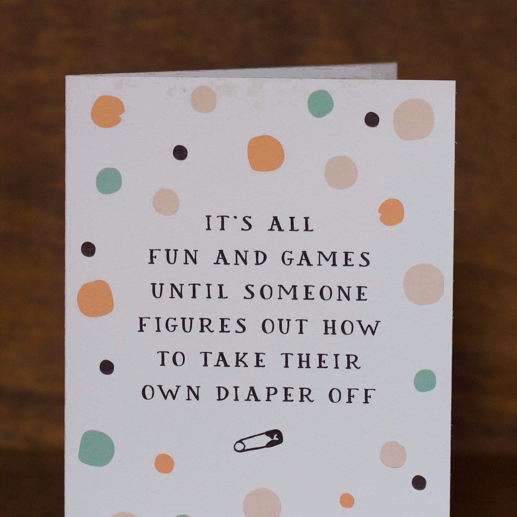 Baby greeting card with polka dot pattern and humorous text on a wooden surface