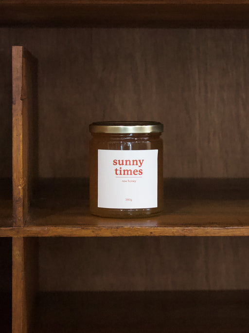 Sunny Times jar of honey with a 'sunny times' label on a wooden shelf