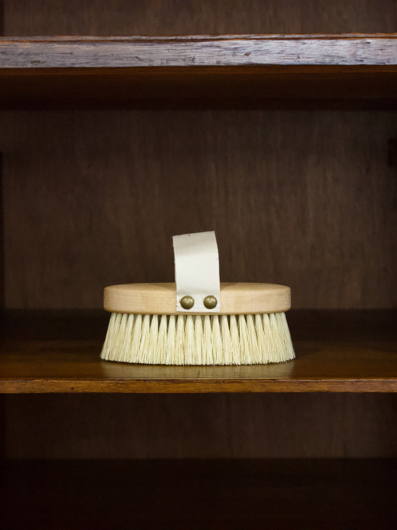 Massage b rush with a wooden handle and bristles on a wooden shelf.