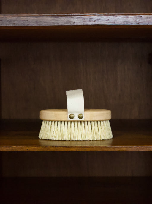 Massage b rush with a wooden handle and bristles on a wooden shelf.