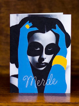 Sympathy greeting cards by Carla Cards with a stylized face design and the word 'Merde' on a wooden surface