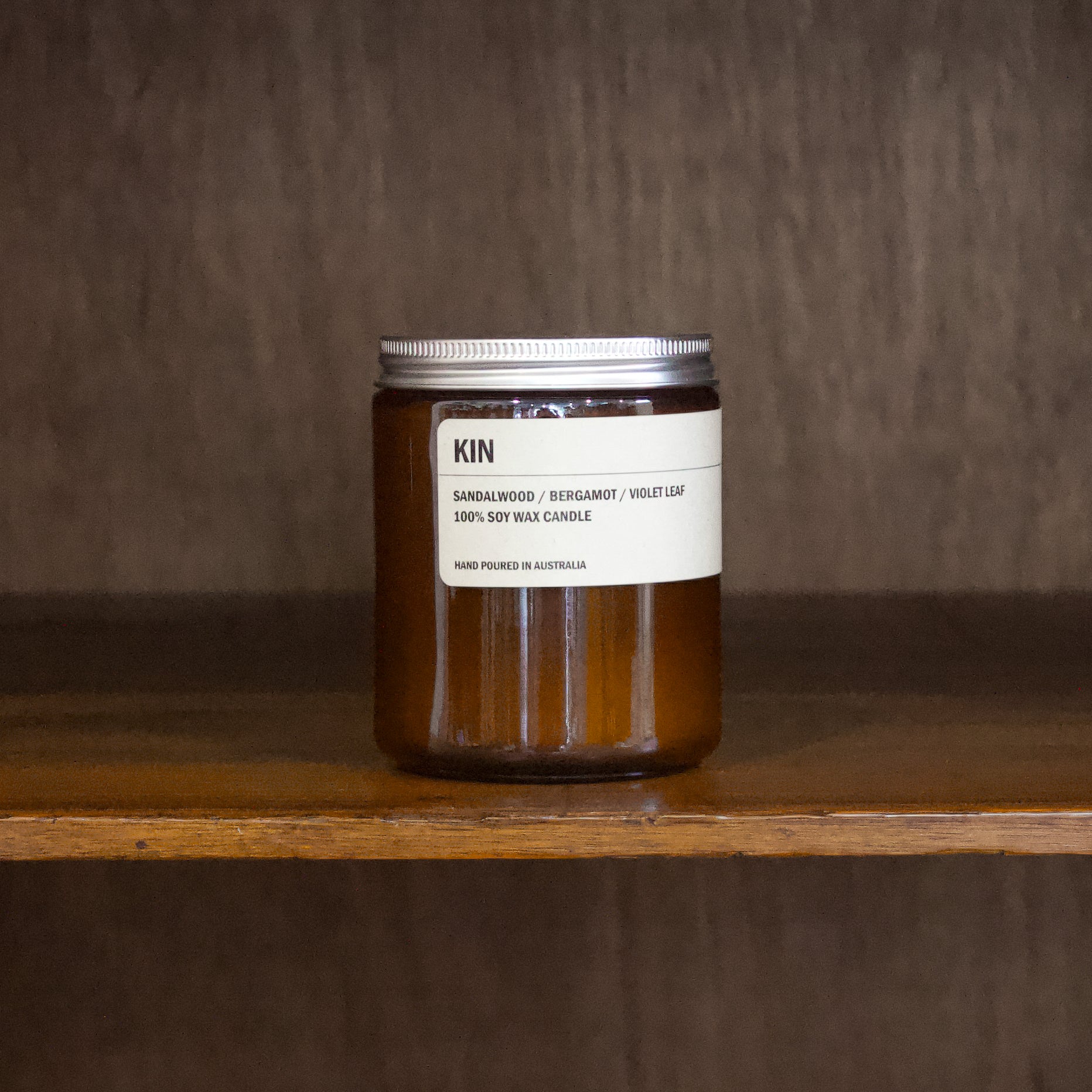Posie candle jar labeled 'KIN' on a wooden shelf with a dark background
